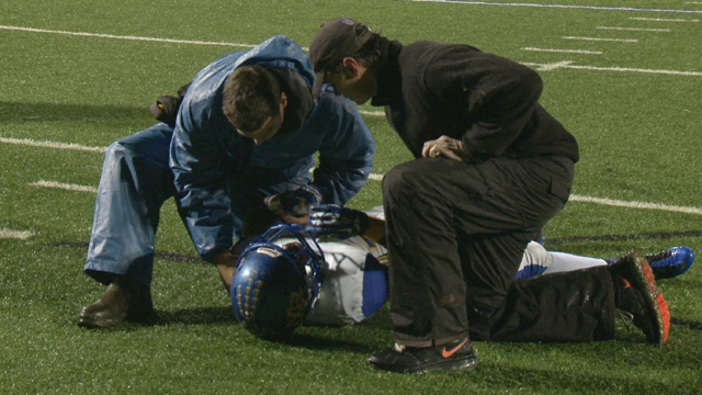 A high school football player being evaluated by athletic trainers after a large impact.